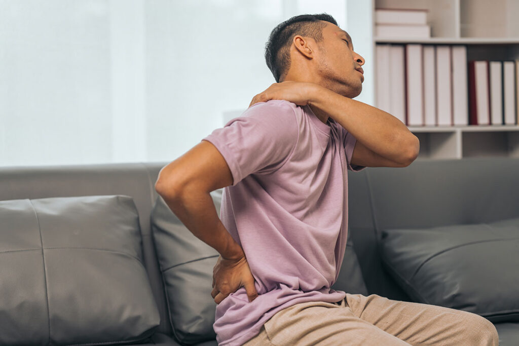 stressed man sitting on a couch sore from back pain and neck pain